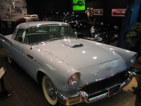 1968 Ford Mustang - A light blue 1955-1957 Ford Thunderbird is displayed in a museum, with a black car visible behind it.