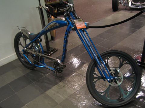 1968 Ford Mustang - A custom blue chopper motorcycle is displayed indoors, a unique front wheel design and a prominent teardrop-shaped gas tank.