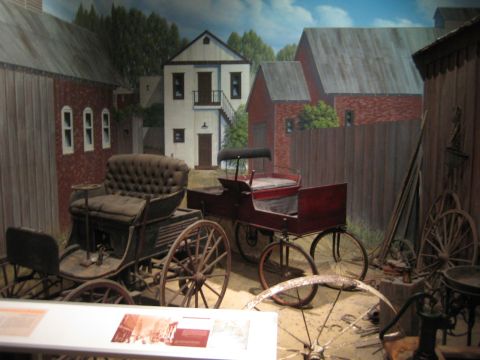 1968 Ford Mustang - A museum exhibit features two vintage horse-drawn carriages set against a painted backdrop of a historical village scene.