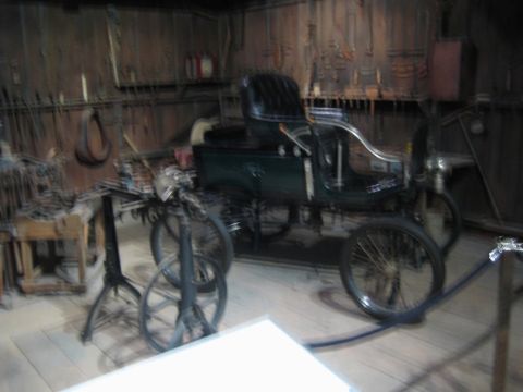 1968 Ford Mustang - An early automobile with a dark green body sits in a rustic workshop setting, surrounded by tools.