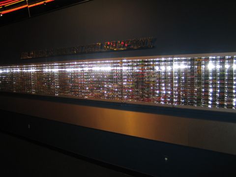 1968 Ford Mustang - A wall-mounted display case showcases a vast collection of small-scale model cars, illuminated by bright lights.