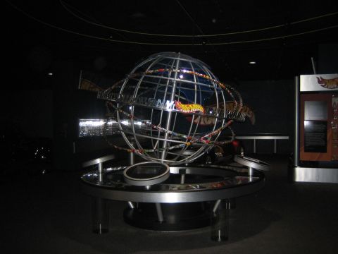 1968 Ford Mustang - A large globe display the Hot Wheels World logo and miniature cars is shown in a museum setting.