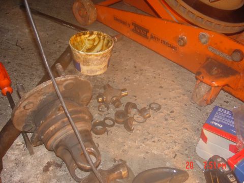 1995 Dodge 1500 - Parts laid out on the floor, including a U-joint, bearings, and a tub of grease, with an orange jack in the background.