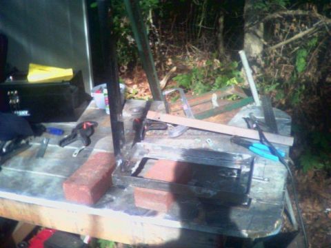 1993 Ford Bronco - Outdoor fabrication in progress on a plywood work table: a rectangular sheet-metal box being welded up for a jerry can carrier, held square…