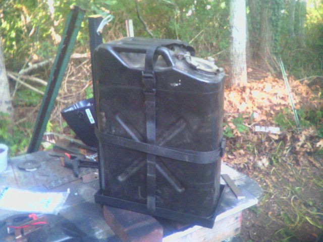 Home-built steel jerry can carrier with strapped black fuel can on outdoor workbench