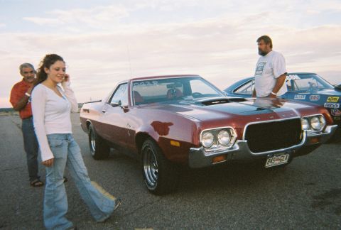 1972 Ford Ranchero - A red 1972 Ford Ranchero is parked next to another vehicle at a drag strip, with people standing nearby.