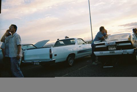 1972 Ford Ranchero - Two pickup trucks are parked side-by-side under a cloudy sky, with people gathered around.