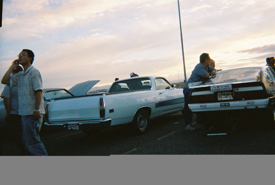 White Ford Ranchero with hood up at evening car meet alongside open-trunk sedan