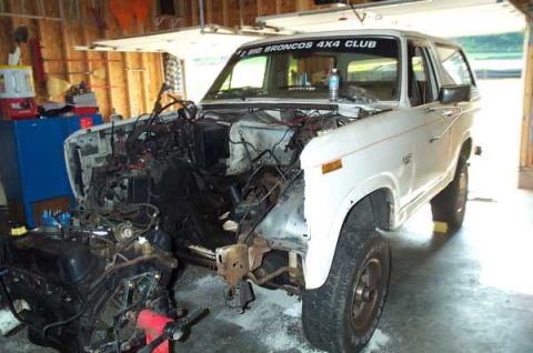 1985 Ford Bronco - 1985 Ford Bronco engine bay is open for repair work in a garage setting.