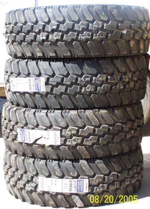 1990 Ford Bronco - Four aggressive mud-terrain tires are stacked vertically with paper labels, dated August 20, 2005.