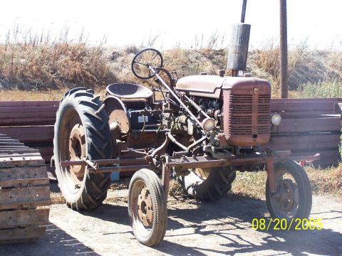 1990 Ford Bronco - weathered rusty antique narrow-front farm tractor with implement bar sits in a yard near stacked steel, dated August 20, 2005.