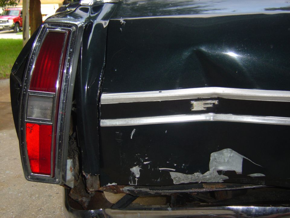 Rear quarter of a black car with vertical taillight, crushed and torn body damage to lower quarter panel