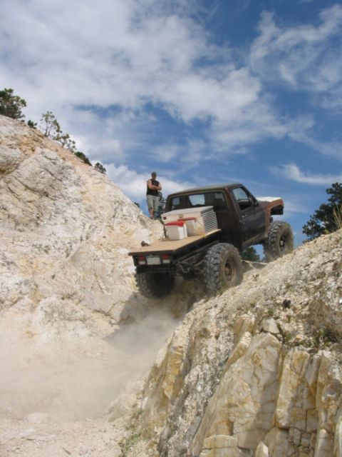 1981 Ford Bronco - A modified truck navigates a challenging off-road trail under a partly cloudy sky.