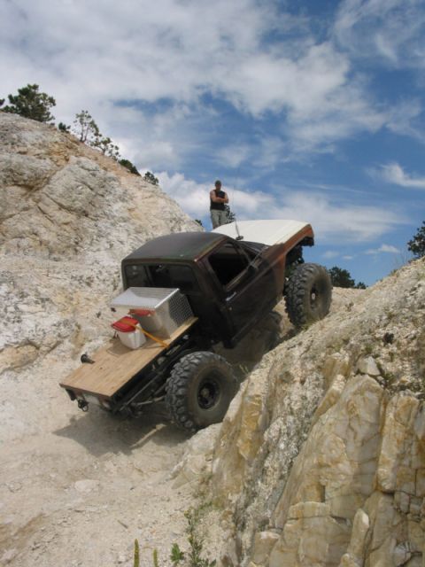 1981 Ford Bronco - A person stands on a rocky hill overlooking a heavily modified off-road vehicle navigating a steep, challenging terrain.