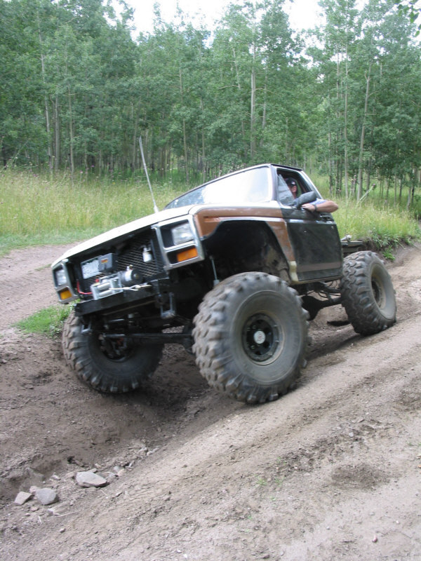 Topless brown Ford 4x4 flatbed with winch flexing through ruts on an aspen forest road