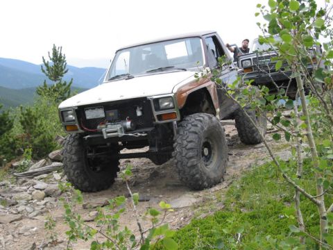 1981 Ford Bronco - Two off-road vehicles navigate a challenging rocky terrain on a mountain trail.