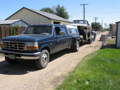 1981 Ford Bronco - A dark blue Ford F-350 dually truck is seen towing a trailer with a lifted vehicle on it.