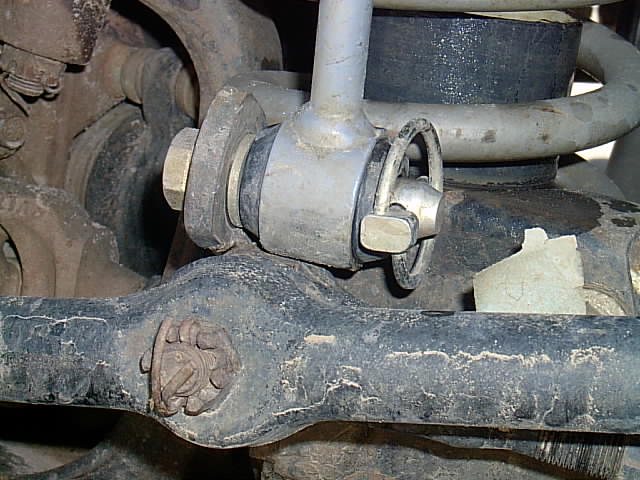 Underbody close-up of a coil spring, track bar bushing and bolt, dusty solid axle suspension