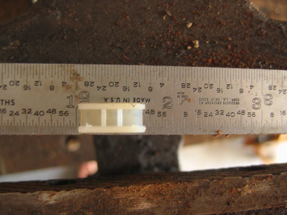 Steel ruler measuring a small white plastic part on weathered wood