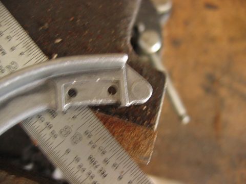 1992 Ford Bronco - A close-up of a small aluminum bracket with two drilled mounting holes and a rounded end, clamped in a vise alongside a steel machinist's r…