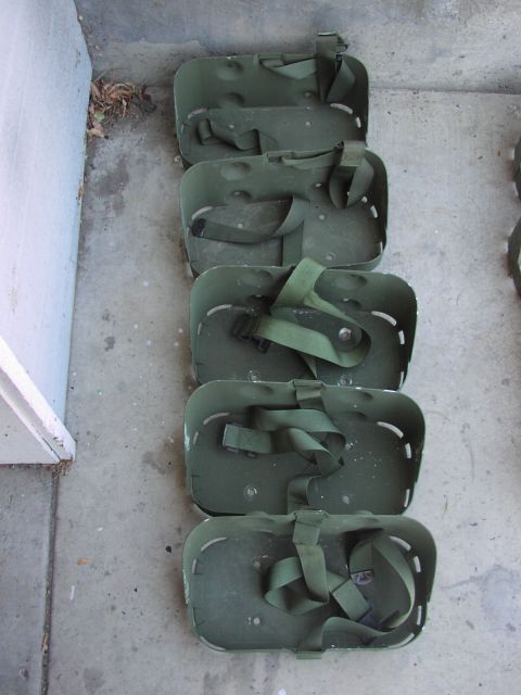 1979 Ford Bronco - Several olive drab carrying frames with green straps are lined up on a concrete surface.