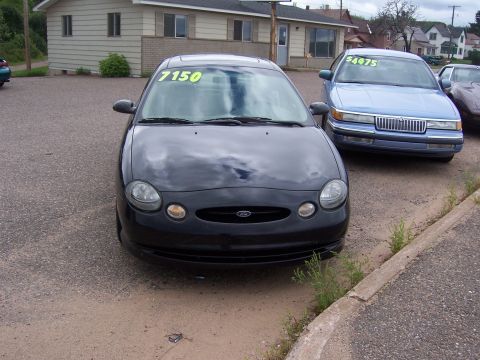 1996 Mercury Sable - A black 1996 Ford Taurus is parked in front of a building, with a blue Mercury Sable behind it.