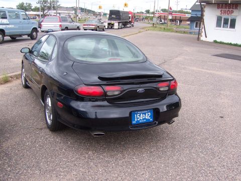 1996 Mercury Sable - Black 1996 Ford Taurus parked on asphalt with other vehicles and buildings in the background.