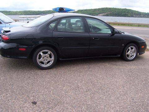 1996 Mercury Sable - A black sedan is parked next to a body of water, with a kayak secured to its roof.