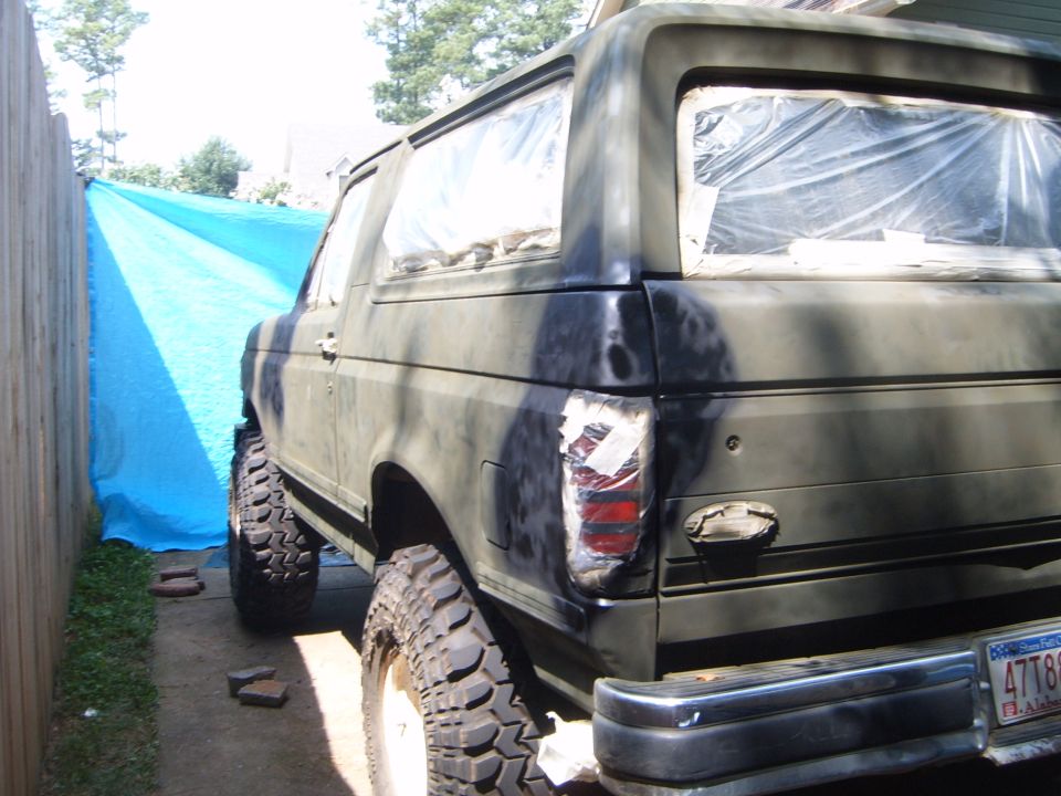 Dark green SUV with camouflage paint, lifted suspension, and off-road tires, rear view