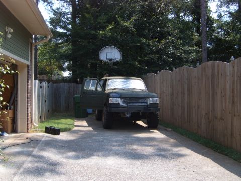 1988 Ford Bronco - A dark green SUV sits in a driveway with its doors open, a basketball hoop visible in the background.