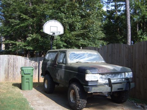 1988 Ford Bronco - 1988 Ford Bronco in camouflage paint, parked outdoors with windows covered in plastic.