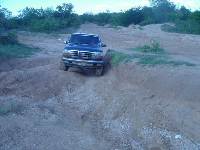 Dark Ford Bronco descending a rutted dirt hill head-on at an off-road area