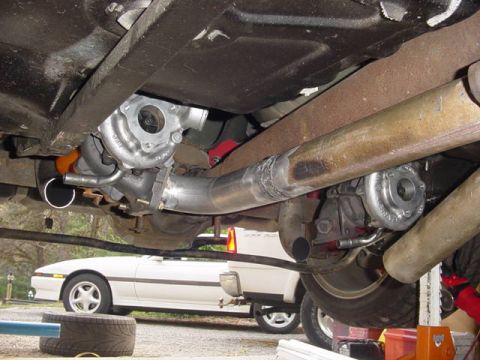 1995 Ford Mustang - The underside of a vehicle shows a newly installed turbocharger and exhaust system, with another car visible in the background.