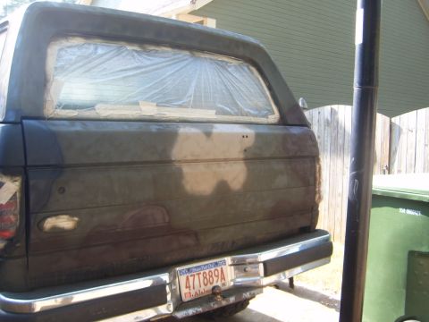 1988 Ford Bronco - The rear of a vehicle is shown with the window covered in plastic and tape, likely in preparation for painting.