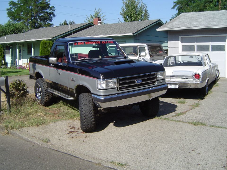 Black-and-silver lifted Ford F-series 4x4 in a driveway beside an old white sedan