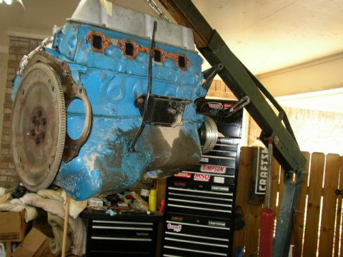 1995 Ford Bronco - A blue engine block is suspended by a hoist, with tool chests and a wooden fence visible behind it.
