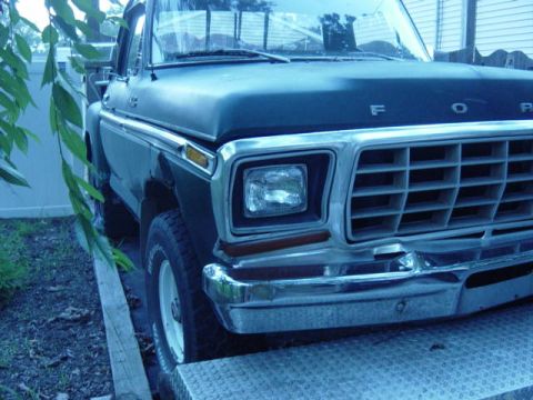 1987 Suzuki Samurai - The front grille and headlight of a classic Ford pickup truck are visible in this close-up shot.