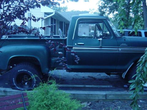 1987 Suzuki Samurai - A dark green pickup truck is parked outdoors, showing its side profile and a flat tire on the front wheel.