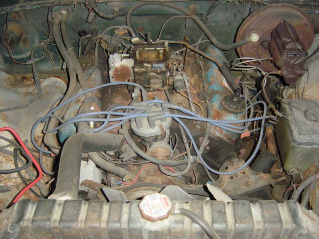 Rusty engine bay with a carbureted blue V8 and front-mounted distributor