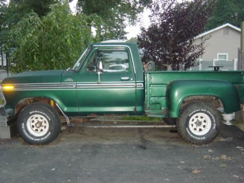1987 Suzuki Samurai - This green pickup truck is parked outside a house with trees and a fence in the background.