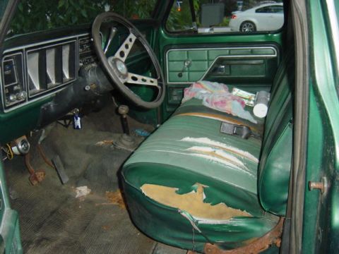 1987 Suzuki Samurai - The worn interior of a green truck features a torn bench seat and a cluttered dashboard.