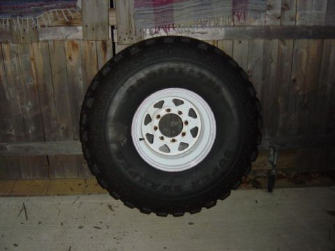 1987 Suzuki Samurai - A single tire and wheel assembly is shown against a rustic wooden background.