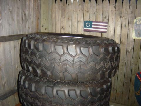 1987 Suzuki Samurai - Two large, knobby off-road tires are stacked in front of a wooden fence.