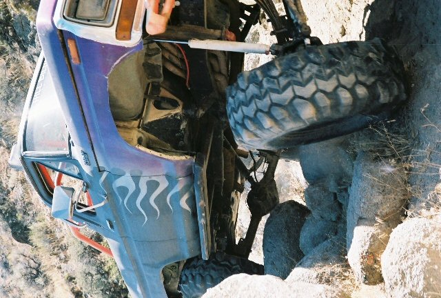 Purple truck with flame decals, lifted suspension, and large off-road tires, stuck on rocks