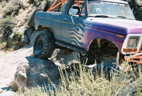 1979 Ford Bronco - This modified 1979 Ford Bronco navigates a rocky trail, its off-road capabilities with flame decals and an orange roll cage.