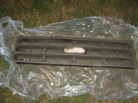 1988 Ford Bronco - A gray plastic grille, likely from a 1987 Ford Bronco, is laid out on plastic sheeting on a grassy area.
