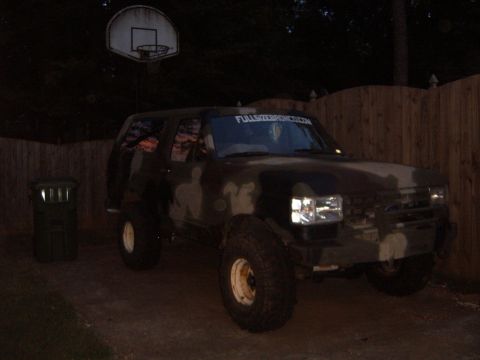 1988 Ford Bronco - 1988 Ford Bronco with camouflage paint is parked outside at dusk.