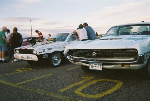 1972 Ford Ranchero - Two cars are parked on a drag strip, one with racing decals and the other a white coupe with a prominent grille.