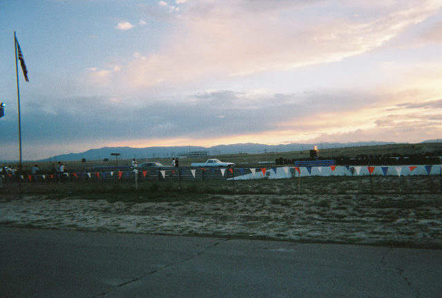 Dusk scene of a pennant-lined event lot with a white classic car and mountains behind