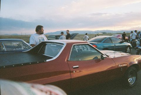1972 Ford Ranchero - A group of people and vehicles are gathered at a drag strip during sunset.